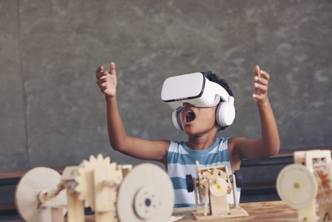 African black boy wearing 3D gadget and looking out above and having the simulation mechanism robot model wooden on table in classroom. why_and_how_to_ensure_digital_accessibility_in_education